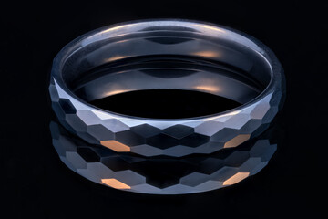 A lit faceted tungsten ring on a black glossy surface.
