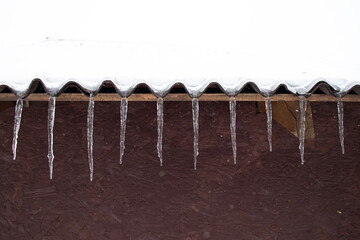 Icicles hanging from snowy roof edge winter freezing weather cold season house building frost ice detail background