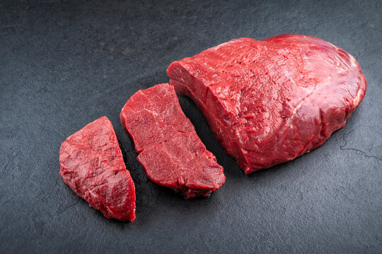 Boneless venison haunch - top round steak raw offered as close-up on slate plate
