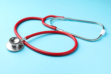 Red stethoscope on light blue background, closeup