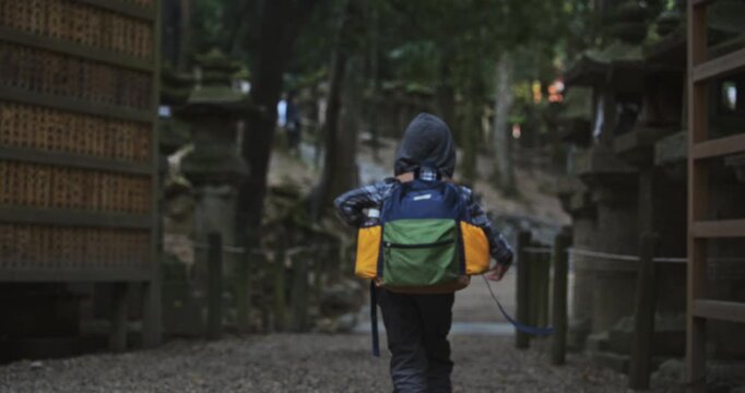 Boy with backpack running off through Japanese shrine area surrounded by autumn trees