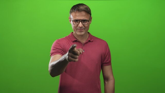 Man pointing finger at camera with hand extended, wearing glasses and red polo shirt in studio; assertive challenge.