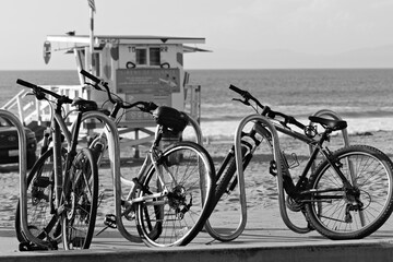 Fototapeta premium Bicycles secured to rack on sandy California beach with lifeguard tower and ocean waves in background.