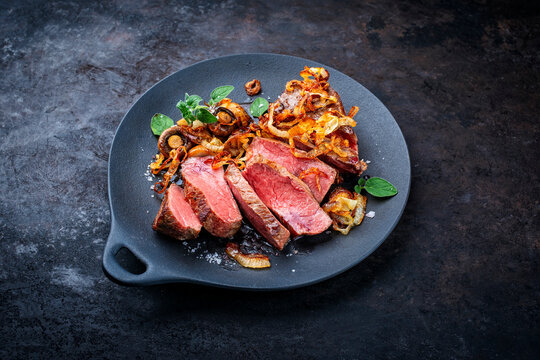 Zwiebelrostbraten roast beef - sirloin beef steak braised with fried onion rings and mushrooms served as close-up on a design plate