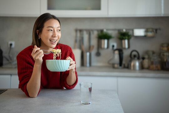 Young asian woman enjoying instant noodles in kitchen