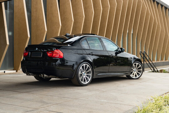 Black BMW M3 E90 rear three quarters view, Sport sedan parked near modern architecture