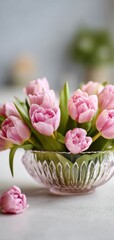 Obraz premium Pink tulips in glass bowl on white table, soft daylight, fresh spring floral home decor scene
