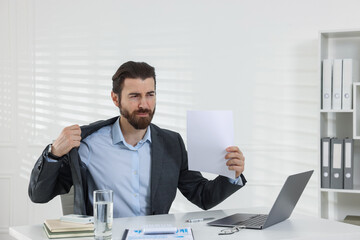 Man suffering from heat at table near white wall indoors