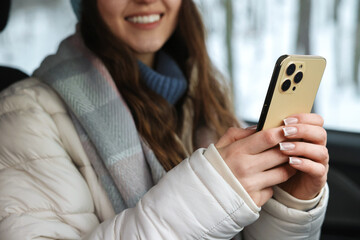 Fototapeta premium Woman with smartphone in car at snowy forest, closeup