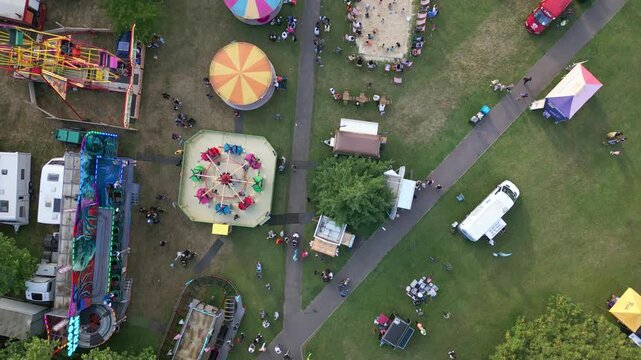 An aerial view of a bustling fairground with rides, stalls, food vendors, and many people enjoying a day out.