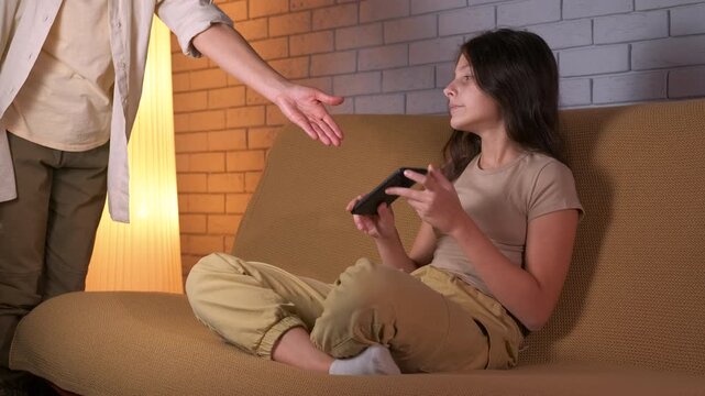 Parent taking smartphone from teenage daughter with addiction. Displeased teenage girl giving her smartphone to her mother, highlighting the issue of gadget addiction, parental control