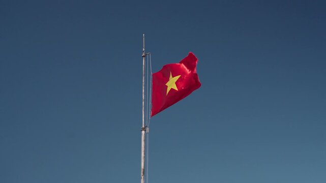Vietnamese national flags waving at Fansipan Peak in Sapa, Vietnam, with visitors at the summit under a clear blue sky, symbolizing national pride, travel, and achievement at Vietnam&rsquo;s highest mountai