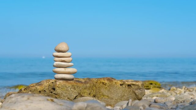 Balanced stone pyramid on a seashore. Serene stack of smooth pebbles balancing on a larger rock on a quiet beach, symbolizing harmony, stability, and tranquility with the calm blue ocean and clear sky