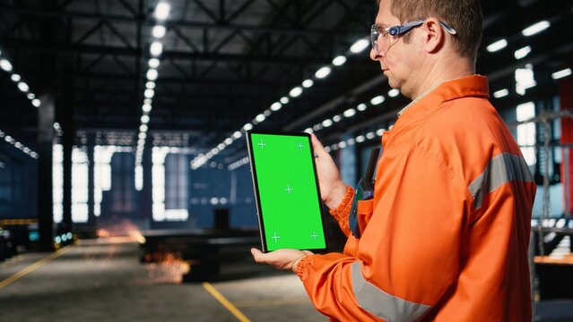 Vertical green screen with worker managing steel operation tasks, surrounded by metal machinery and fabrication tools within the warehouse facility. Engineering through manpower.