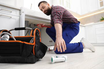 Plumber with wrench taking siphon from floor indoors, low angle view