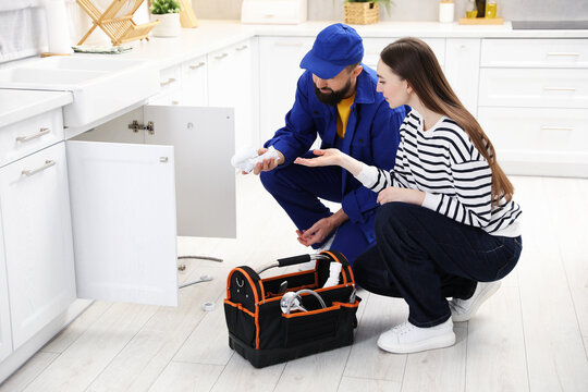 Young woman talking with plumber in kitchen