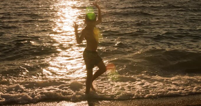 Young boy in silhouette enjoys throwing stones into the ocean at a beautiful sunset.