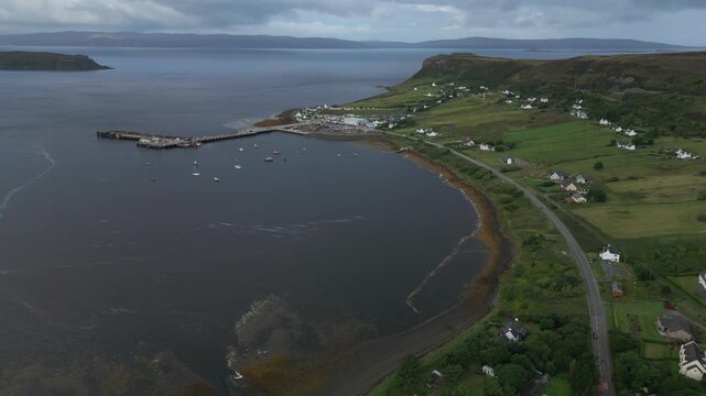 Aerial view of a coastal village with a harbor and houses nestled in green hills.
