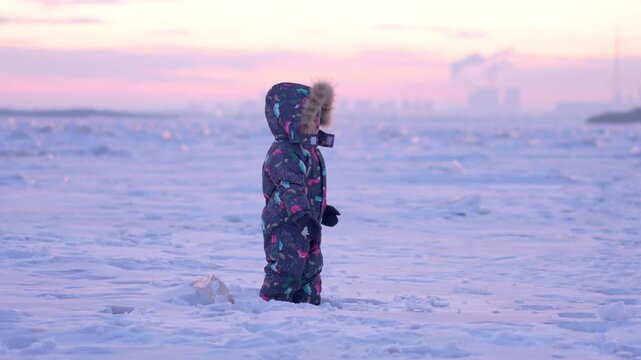 Child wandering the icy landscape as the industrial skyline fades into sunset colors