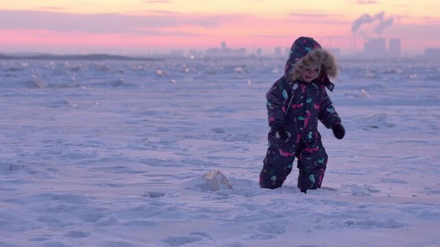Child wandering the icy landscape as the industrial skyline fades into sunset colors
