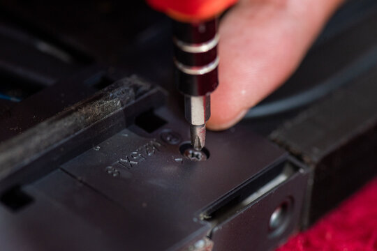 Closeup of someone using a screwdriver to tighten a screw in dark plastic. Suitable for construction, engineering, repair themes.