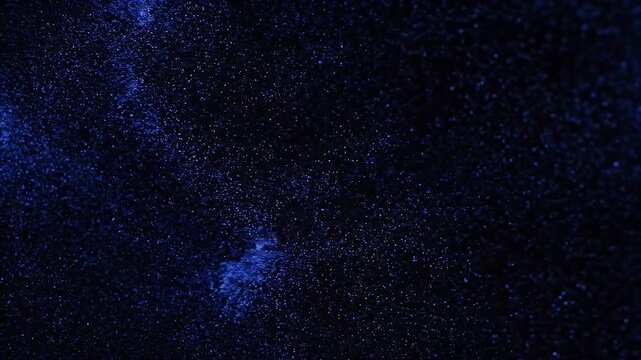 A close-up, textured view of tiny bright blue particles scattered across a dark background