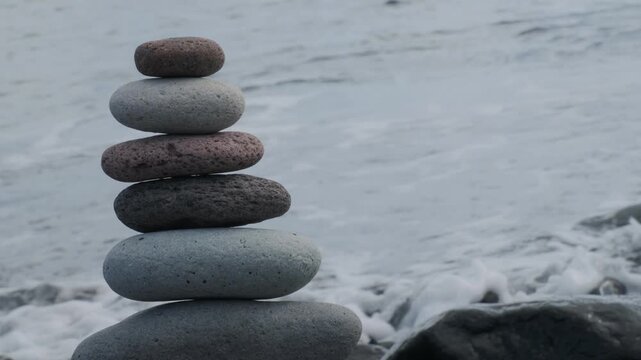 male hand carefully stacks Smooth zen-like pebbles, balanced pyramid against ocean waves, sea therapy on beach, Meditation and mindfulness, harmony, travel, and serenity coastal retreats