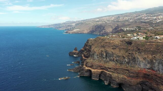 Aerial drone flight over northern Tenerife coastline towards Roque El Cagado with villages and volcanic landscape
