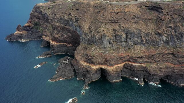 Rotating aerial drone shot over Roque El Cagado cliffs with clear Atlantic Ocean waters in Tenerife
