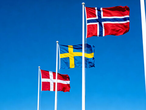 Three Scandinavian flags, Denmark, Sweden, and Norway, flying proudly against a vibrant blue sky on tall white flagpoles.
