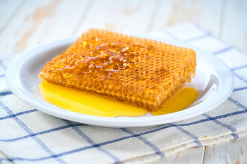 Sweet golden bee honey dripping out of honeycomb in a plate, selective focus.