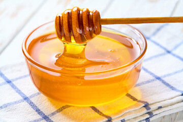 Natural honey in a glass bowl on a light kitchen table, selective focus.