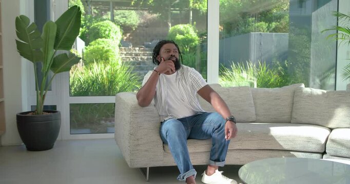 African adult man receiving phone call, answering and responding to funny caller on sectional sofa