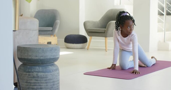 African girl in pink top steadying shifting into lunge, stretching hamstring on purple mat at home