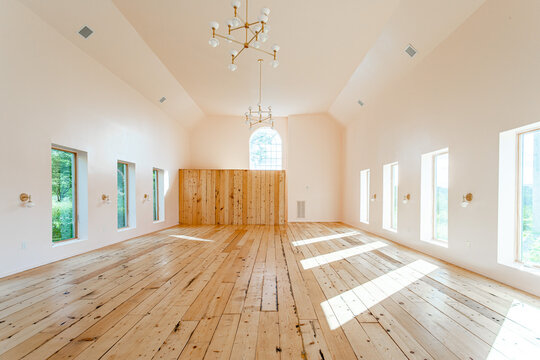Renovated barn interior with vaulted ceiling and wide plank wood floors, bright minimalist open space with tall windows and modern chandeliers