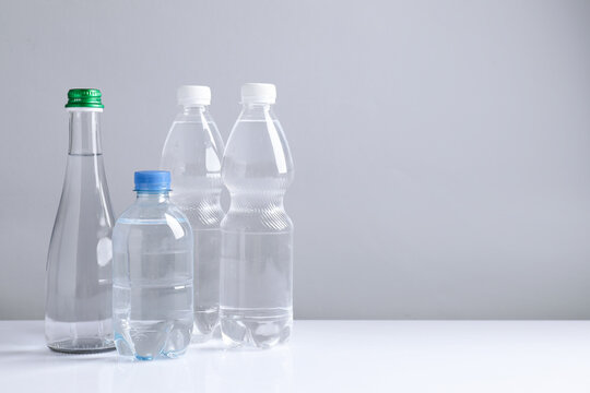 Water bottles of different sizes on white table against grey background, space for text