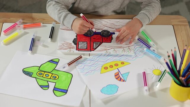 Little boy drawing car with felt tip pen at wooden table indoors, closeup