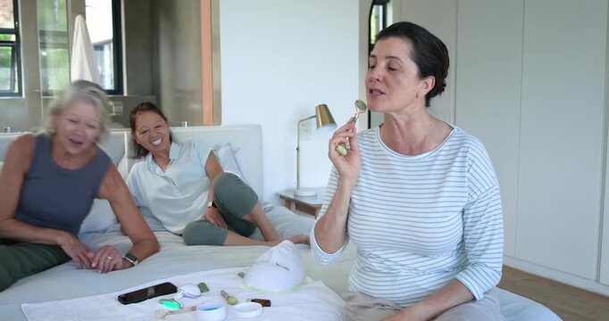 Diverse women with senior, main woman reaching jade roller on bed teaching routine, copy space