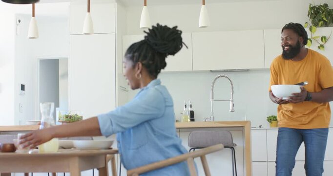 Couple at table woman clapping as man walking from kitchen carrying white bowl to serve meal