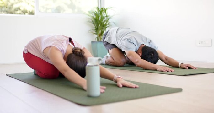Diverse pair folding into child's pose, session start and deepening hold in studio near teal bottle