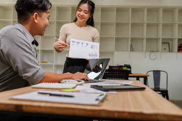Obraz premium Two people are looking at a table with a laptop, a tablet, and a calculator. They are pointing at a graph on the tablet 