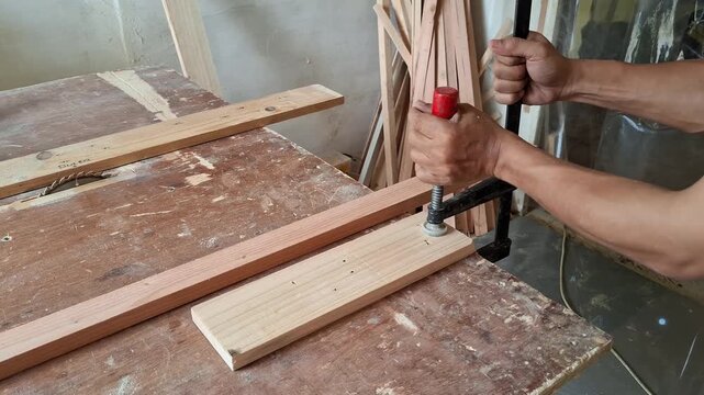 A carpenter is took off f-clamp to the wooden board.