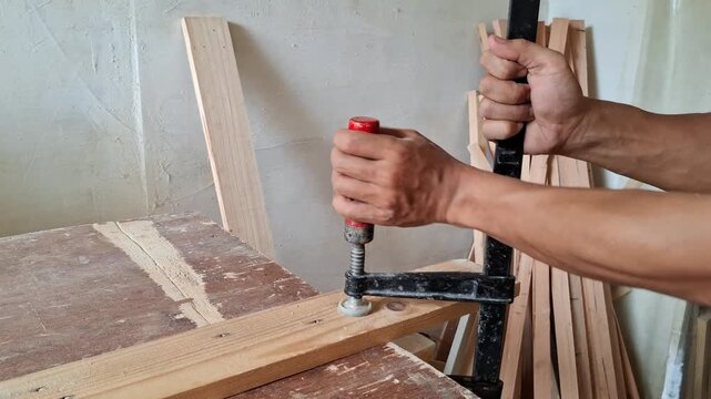 A carpenter is installing clamp to the wooden board.