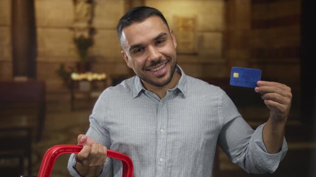 Smiling man gently holds creditcard and bright red handtruck handle in church aisle; charity generosity joy.