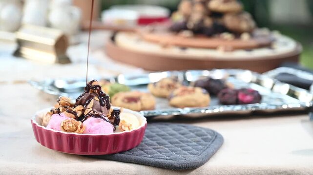 Ice cream chocolate sauce hot fudge strawberry walnut dessert in ramekin with drizzle and scoop, cookie on tray, rich syrup pouring over pink scoops, nut crunch, outdoor table, natural light