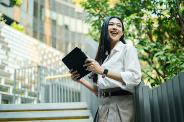 Portrait of a successful asian business woman using phone or digital tablet in front of modern...