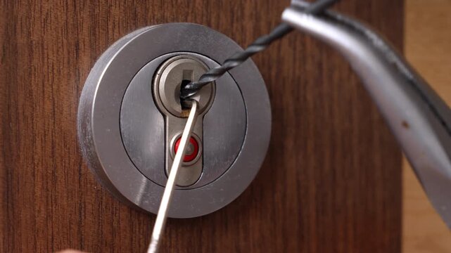 A close-up image showing a metal lock on a wooden door being manipulated by a pick tool inserted into the keyhole, suggesting a lockpicking activity in progress