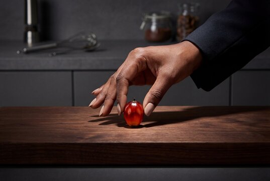 Woman hand carefully placing single red palm oil fruitlet on dark wooden surface