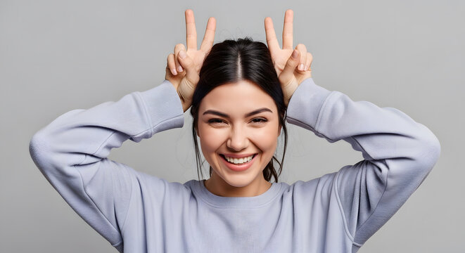 A smiling young woman posing with her fingers making bunny ears on her head