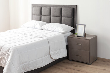 Interior of a modern bedroom with a grey bed featuring a cozy blanket and a wooden bedside table, padded headboard © Jesus